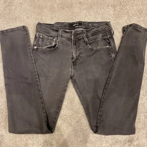 Replay Anbass Jeans - Svarta Replay Hyperflex jeans med skinny passform och klassisk femficksdesign. Jeansen har en lätt tvättad look, dragkedjegylf och stretchigt material för extra komfort. Snygga detaljer på bakfickan och diskret Replay-logga vid fickan.