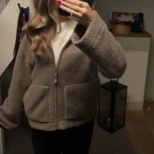 Beige teddyjacka med dragkedja - Mysig beige teddyjacka med hög krage och dragkedja framtill. Jackan har två stora fickor och en avslappnad passform. Perfekt för kyliga dagar när du vill vara både varm och snygg.