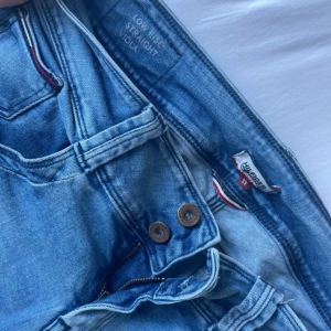 Tommy Hilfiger ljusblå straight jeans - Snygga ljusblå jeans från Tommy Hilfiger med låg midja och straight fit. Klassisk femficksmodell med Hilfiger-detalj på bakfickan och dubbla knappar i midjan. Jeansen har en fräsch tvätt och är tillverkade i mjukt denimtyg. W27 L32 postar inom 24 timmar💕💕