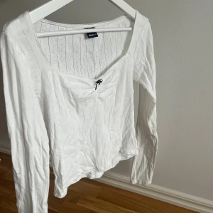 Pyjamas tröja - Säljer en vit långärmad topp från Gina Tricot med subtila vertikala ränder och små hålmönster. Toppen har en v-ringad hals med en liten svart rosett framtill. Mjuk och skön bomullskänsla, perfekt för dig som gillar enkel men söt stil.