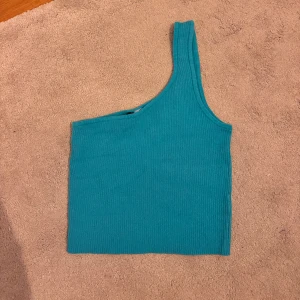 Turkos ribbad oneshoulder topp - Säljer en turkos ribbad topp med oneshoulder-design. Toppen är ärmlös och har en tight passform som sitter snyggt på kroppen. Perfekt för dig som vill sticka ut.