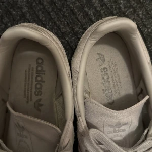 Adidas Samba Cordura sneakers ljusgrå - Adidas Samba sneakers i ljusgrå färg med Cordura-material för extra slitstyrka. Klassisk låg modell med snörning, rund tå och svart platt sula. Ikoniska tre ränder på sidan och diskret Adidas-logga på plösen. Perfekt för dig som gillar stilrena och tåliga sneakers.