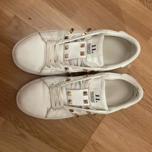 Valentino Rockstud liknande vita sneakers - Säljer ett par vita Valentino Garavani Rockstud liknande sneakers med coola guldfärgade nitar och snörning. Riktigt sköna skor! Knappt använda  . Kontakta gärna för frågor! Tillkommande lite påpucklad box