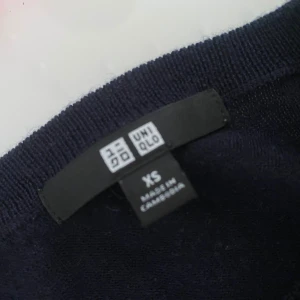 Mörkblå kashmirtröja från Uniqlo XS - Snygg mörkblå rundhalsad tröja från Uniqlo i mjuk merino. Klassisk modell med långa ärmar och ribbade muddar vid hals, ärmslut och nederkant. Perfekt för dig som gillar stilrena och bekväma plagg med lyxig känsla.