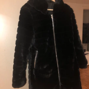 Svart pälsjacka med dragkedja - Mysig svart pälsjacka med lång ärm och snygg dragkedja framtill. Jackan har en fluffig känsla och är perfekt för kalla dagar. Fodrad insida och två fickor med dragkedja. Snygg och stilren look som passar till det mesta.