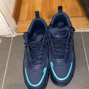 Nike Air Max 90 blå sneakers strl 38 - Säljer ett par Nike Air Max 90 sneakers i marinblått med turkosa detaljer. Skorna har snörning, platt sula och är tillverkade i syntetmaterial och textil. Ikonisk Air Max-dämpning och cool design med tydliga Nike-loggor på plös och innersula.