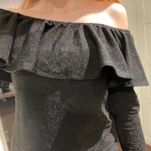 Svart-glittrig volangtopp, Offshoulder  - Säljer en svart långärmad glittrig tröja ifrån H&M. Tröjan är off shoulder och har silverglitter. Det är en perfekt festtopp nu till höst/vinter för att den är lite varmare pga dom långa ärmarna. Tröjan är ju även perfekt till Nyår!! Hör av er vid frågor Osv!!❤️Priset kan även diskruteras!!