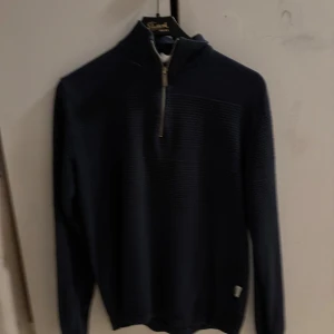 Mörkblå stickad tröja Selected Homme - Mörkblå stickad tröja från Selected Homme med snygg struktur och half zip-dragkedja i halsen. Tröjan har lång ärm och ribbade muddar, perfekt för lager på lager under kyliga dagar.