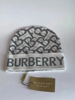 Gråvit Burberry mössa med hjärtan - Snygg mössa från Burberry i grått och vitt med hjärtmönster och stor logga framtill. Mössan är stickad och har en bred uppvikt kant. Perfekt för dig som vill ha en cool accessoar med lyxig känsla.