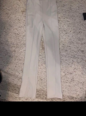 Beige ribbade byxor med slits från H&M - Säljer ett par beige ribbade byxor från H&M i storlek S. Byxorna har hög midja, raka ben och snygga slitsar framtill vid bensluten. Materialet är mjukt och stretchigt, perfekt för en chill och trendig look. Bra för priset 