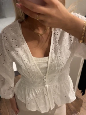 Viral Zara blus - Supersöt vit broderad topp som var viral i somras 🌼 Figurnära upptill med markerad midja och peplum som ger jättefin passform. Djupare v-ringning med klädda knappar framtill. Funkar lika bra till jeans som till linnebyxor eller kjol. Perfekt till sommar, semester eller som en romantisk vardagstopp ✨ Säljer pga kommer inte till användning. OBS prislapp kvar!!