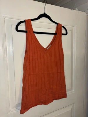 Orange ribbad linnetopp STOCKH LM - Säljer en ribbad linnetopp i en snygg orange färg från STOCKH LM. Toppen har v-ringning och är ärmlös med breda axelband. Materialet är mjukt och stretchigt, perfekt för varma dagar eller som layering-piece.