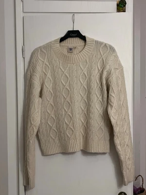 Beige stickad tröja från Marie Serneholt - Säljer en beige stickad tröja från Marie Serneholt som är köpt på Ullared! Grovt kabelstickat mönster och ribbade muddar vid hals, ärmslut och nederkant. Tröjan har rund hals och lång ärm, perfekt för kyliga dagar. Supermysig och snygg att matcha med jeans eller kjol. Använd fåtal gånger! 