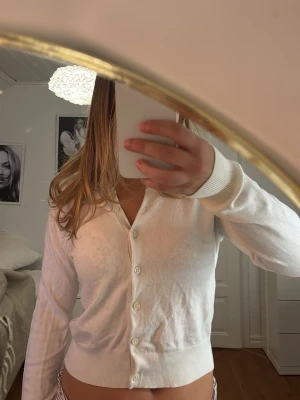 Vit kofta från H&M i storlek S - Säljer en klassisk vit kofta från H&M i storlek S. Koftan har långa ärmar, ribbade muddar och knappar framtill. Perfekt att slänga över en topp när det är lite kyligt. Mjuk och skön kvalitet som känns lätt mot huden.