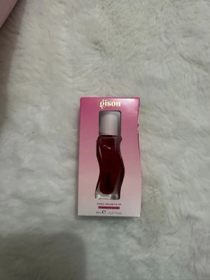 Gisou Honey Infused Lip Oil Strawberry - Säljer en Gisou honey infused lip oil i färgen Strawberry Sorbet. Kommer i en snygg vågformad genomskinlig flaska med ljusrosa lock. Läppoljan har en djup röd nyans och innehåller honung för extra fukt och glans. Perfekt för dig som vill ha mjuka och glansiga läppar med en hint av färg.