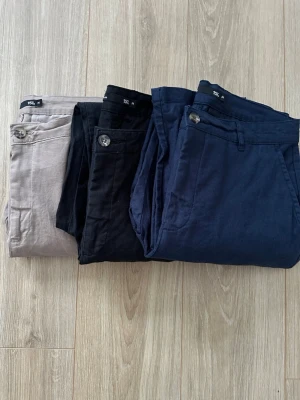 3-pack chinos i olika färger, strl M - Säljer tre par chinos i storlek M, i färgerna beige, svart och mörkblå. Byxorna har klassisk passform med knapp och dragkedja framtill samt bälteshällor. Materialet känns mjukt och lätt, perfekt för en clean och stilren look. 200kr för alla 3. 