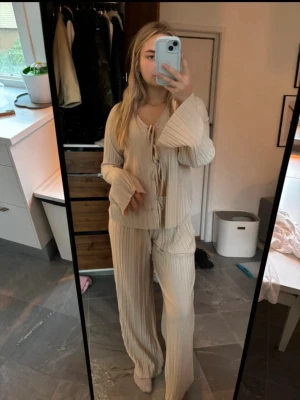 Beige set från bubbleroom  - Säljer ett par beige plisserade byxor med bred passform och hög midja. Byxorna är tillverkade i ett mjukt och flowy material som ger en chill och trendig vibe. Perfekta för dig som gillar en avslappnad men ändå stilren look.