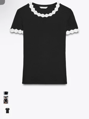 Svart t-shirt med vita blommiga detaljer - Svart t-shirt med korta ärmar och vita blommiga spetsdetaljer runt halsringningen och ärmsluten. Sitter figurnära och har en stilren, modern look som passar perfekt till kjol eller jeans.från Zara 