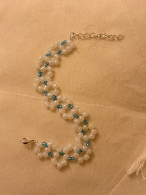 Vit och blå pärlväst med kedja - Säljer en handgjord pärlväst med vita och blå pärlor i ett snyggt mönster. Västen har en silverfärgad kedja och lås för enkel på- och avtagning. Perfekt för dig som vill sticka ut med något unikt och färgglatt.