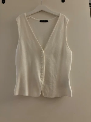 Vit stickad väst från Gina Tricot - Säljer en stilren vit stickad väst från Gina Tricot med v-ringning och knappar framtill. 
