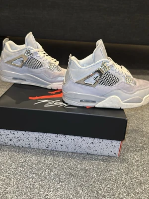 Nike Jordan 4 i ljusgrå mocka - Säljer ett par Nike Jordan 4 sneakers i ljusgrå mocka med silvriga detaljer och meshpaneler på sidorna. Skorna har snörning, platt sula och rund tå. Ikonisk Jumpman-logga på plösen och hälen. Kommer med originalkartong.