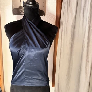 Mörkblå omlott korsettopp BikBok - Snygg mörkblå korsettopp från BikBok i omlottmodell med halterneck. Toppen har glansigt tyg framtill och smockad baksida som ger en tight passform. Perfekt för dig som vill ha en trendig och stilren look.