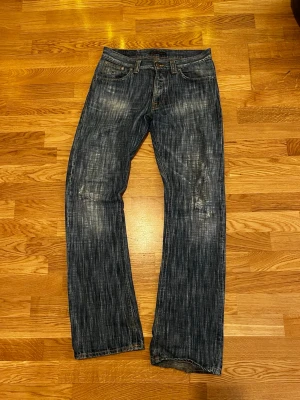 Nudie Jeans Regular Ralf 30/34 - Säljer ett par Nudie Jeans Regular Ralf i tvättad mörkblå färg med coolt slitet mönster. Klassisk femficksmodell med raka ben och orangea sömmar. Tillverkade i 100% bomull för skön känsla och snygg passform.