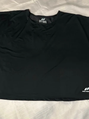 Svart tränings-tshirt Pro Touch L - Svart tränings-tshirt från Pro Touch i storlek L. Tillverkad i lätt och ventilerande syntetmaterial med DRYPLUS-teknologi. Prickigt meshfoder på insidan för extra andningsförmåga. Perfekt för dig som gillar att träna och vill ha en bekväm t-shirt.