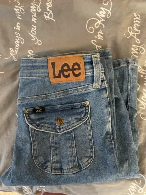 Blå bootcut Lee jeans med ficklock - Säljer ett par klassiska blå Lee jeans med snygga ficklock bak och Lee-logga på både knapp och etikett. Jeansen har raka ben och normal passform, tillverkade i slitstarkt denim med kontrastsömmar. Perfekta för dig som gillar vintagevibbar och coola detaljer. Dom har använts 2 gånger och är i perfekt skick 💕köpte dom för 1,200kr