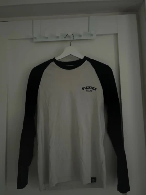 Svartvit långärmad t-shirt Dickies - Säljer en svartvit långärmad t-shirt från Dickies i storlek XS. Klassisk baseballmodell med svarta ärmar och vit kropp, samt Dickies-logga tryckt på bröstet. Tillverkad i mjuk bomull som är skön att bära hela dagen. Lite mässfärgad vid kragen och nån liten fläck på magen