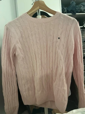 Ljusrosa stickad tröja Subdued  - Säljer en ljusrosa stickad tröja från Subdued i storlek M men passar mig som är S. Tröjan har ett klassiskt kabelstickat mönster, rund hals och ribbade muddar vid ärmslut och nederkant. Liten svart stjärndetalj på bröstet. Perfekt för mysiga dagar.