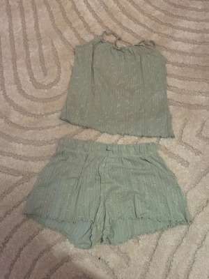 Grön blommig linnetopp med volang - Säljer en ljusgrön linnetopp med tunna axelband och små blommor i mönstret. Toppen har volangkant nedtill och är gjord i ett mjukt, ribbat material som känns skönt mot huden. Perfekt för varma dagar eller som ett mysigt set. Lappen är inte kvar.