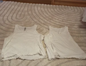 Två vita spetslinnetoppar 158/164 - Säljer två vita linnetoppar i mjuk bomull med spetsdetaljer och vågig kant nertill. Båda har ett diskret hålmönster och en liten rosett framtill på ena toppen. Perfekta till sommaren och lätta att matcha med allt. En är i storlek 146-152 man kan köpa en det  pyamaslinnen men de gr jättebra att använda de till annat