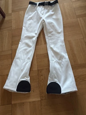 Vita täckbyxor från 8848 Altitude - Säljer ett par vita täckbyxor från 8848 Altitude med svarta förstärkningar vid bensluten och svart bälte med logga. Byxorna har bootcut-snitt, dragkedjor vid bensluten och är gjorda i ett slitstarkt syntetmaterial som passar perfekt för vintern.  Det finns slitning vid både rumpan och knän men inget som syns så bra! Nypris: 2200kr