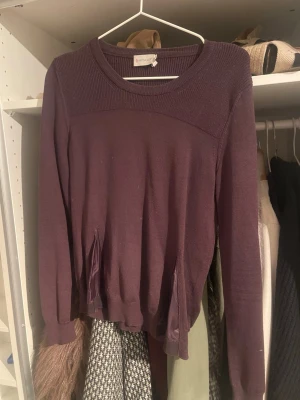 Mörklila stickad tröja från Moncler - Säljer en mörklila stickad tröja från Moncler med rund hals och ribbade detaljer upptill. Tröjan har långa ärmar och coola sidopaneler i blankt tyg som ger en snygg kontrast. Moncler-logga på ena ärmen. Perfekt för dig som gillar exklusiva märken och stilren design.