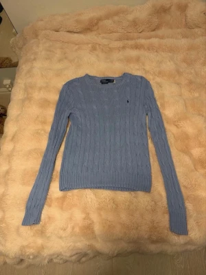 Ljusblå stickad tröja Polo Ralph Lauren - Säljer en ljusblå kabelstickad tröja från Polo Ralph Lauren i storlek M. Tröjan är gjord av mjuk pima bomull, har lång ärm och rund hals. Har nog använt den typ en gång för två år sedan, annars är den inte använd. Nypris ca 2000kr.