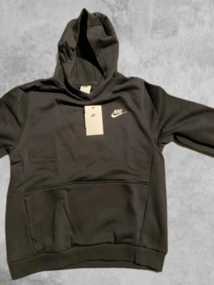 Helt ny svart nike hoodie - Svart hoodie från Nike i storlek XL, med klassisk vit Nike-logga på bröstet. Tröjan har huva, känguruficka och är tillverkad i mjukt material som känns skönt mot huden. Perfekt för chill dagar eller när du vill ha en clean streetstyle. Storlek 158-170.