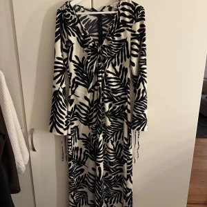 Svartvit långklänning med bladmönster - Snygg långklänning med svart och vit bladmönster, v-ringad framtill och långa ärmar.
