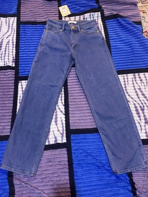 Blå raka jeans från Stylein - Snygga blå jeans från Stylein i modellen Kasey. Jeansen har klassisk femficksdesign, raka ben och guldfärgade nitar vid fickorna. Tillverkade i slitstark bomullsdenim med en ren och tidlös look. Perfekta för dig som gillar enkel och stilren denim.
