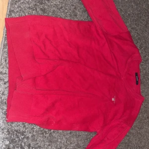 Röd stickad tröja från GANT - Säljer en klassisk röd stickad tröja från GANT i storlek S. Den är ganska stor för mig (175 cm + 60 kg). Tröjan har rund halsringning, långa ärmar och ribbade muddar vid ärmslut och nederkant. Perfekt för dig som gillar stilrena och tidlösa plagg.