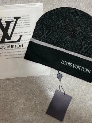 Svart mössa med logga - Snygg svart mössa med klassiskt monogrammönster och tydlig logga framtill. Mössan har en grå rand och är tillverkad i mjukt material som håller dig varm. Perfekt accessoar för att lyfta din stil.