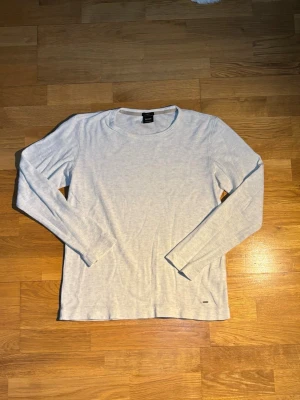 Ljusgrå långärmad tröja Hugo Boss - Säljer en stilren ljusgrå långärmad tröja från Hugo Boss i slim fit. Tröjan är enkel och clean med rund halsringning och mjukt material som känns skönt mot huden. Perfekt till jeans eller chinos för en avslappnad look.