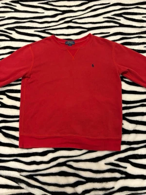 Ralph Lauren - Säljer en röd sweatshirt från Polo Ralph Lauren med klassisk rund hals och långärmad design. Tröjan har ett litet blått broderat logomärke på bröstet och är tillverkad i mjuk bomull. Perfekt för chill dagar och enkel att matcha med jeans eller joggers. Storleken är i kids L (14-16) vilket blir XS i vuxen. Hör av dig vid minsta fundering 😀 