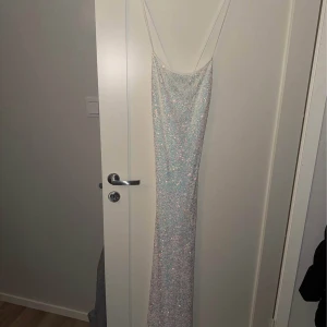 Glittrig långklänning från Bubbleroom - Supersnygg långklänning från Bershka med tunna axelband och öppen rygg. Klänningen är täckt av glittriga paljetter i ljusa toner och har en figurnära passform. Perfekt för dig som vill sticka ut och glänsa! Materialet är syntet och känns lyxigt mot huden.