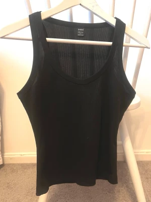 Svart ribbad linnetopp - Säljer en svart ribbad linnetopp i storlek S. Toppen är ärmlös med breda axelband och har en rundad halsringning. Materialet är mjukt och stretchigt, perfekt för att styla med jeans eller kjol. Enkel och stilren design som funkar året runt.