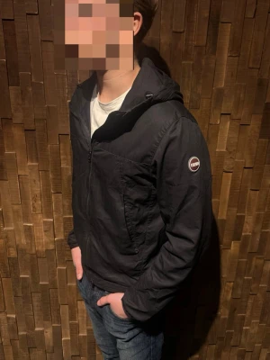 Svart vindjacka från Colmar - Säljer en svart vindjacka från Colmar med huva och dragkedja framtill. Perfekt för dig som vill ha en stilren och funktionell jacka till vardags. Materialet är lätt och smidigt. Det finns inga defekter på jackan! Jackans nypris ligger på 2500kr! Modellen är 180 cm och väger 73kg! Hör av dig vid intresse! (Pris går att diskutera)