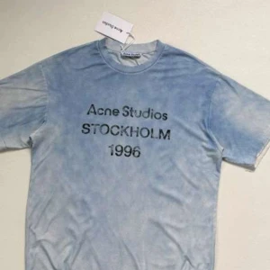 Blå Acne Studios Stockholm - Säljer en ljusblå t-shirt från Acne Studios med tryck 'Acne Studios STOCKHOLM 1996' på bröstet. T-shirten har klassisk passform och korta ärmar. Perfekt för dig som gillar stilrena och trendiga plagg. Passar både till tjejer och men. Helt nya lappar sitter kvar, de är även äkta.