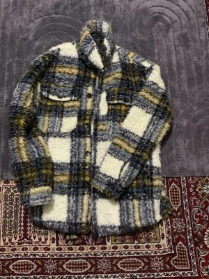 Rutig teddyjacka från Zara, M - Säljer en sjukt mysig teddyjacka från Zara i storlek M. Jackan har ett rutigt mönster i vitt, blått, grått och gult, med stora fickor och knappar framtill. Perfekt för dig som gillar oversized och fluffiga jackor med coola detaljer.