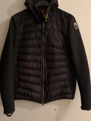 Svart pufferjacka från Parajumpers M - Säljer en svart pufferjacka från Parajumpers i storlek M. Jackan har quiltad front, mesh-liknande ärmar och axlar, dragkedja framtill och bröstficka med dragkedja. Klassisk patch på ärmen och cool gul detalj vid kragen. Perfekt för kyliga dagar.