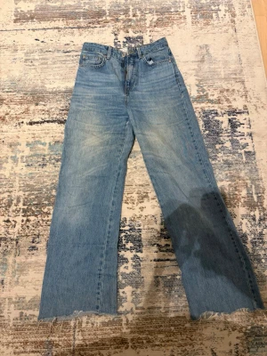 Blå straight fit jeans från Stradivarius - Säljer ett par blå jeans från Stradivarius i modellen long straight fit. Jeansen har hög midja, raka ben och råa, fransiga kanter nedtill. Materialet är klassisk denim i bomull och de har en cool sliten detalj på ena benet. Perfekt för dig som gillar avslappnad stil.